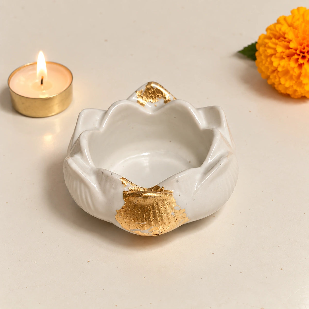 White concrete lotus-shaped tealight holder with elegant gold accents, styled with a lit tealight and marigold flower.