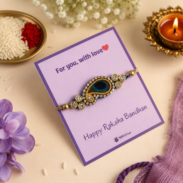 Regal Peacock Rakhi featuring a peacock-inspired centerpiece with blue stones and crystal embellishments, elegantly displayed on a premium Raksha Bandhan greeting card with festive décor.